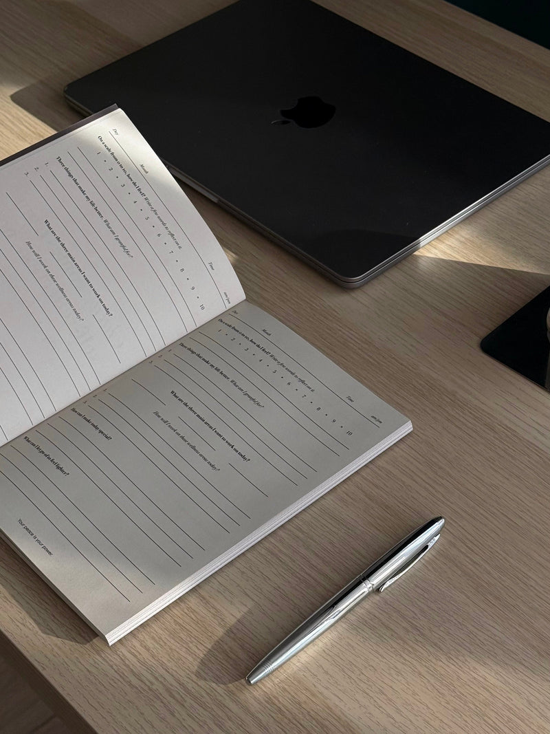 An open journal with a handwritten self-reflection prompt beside a pen in soft natural light.