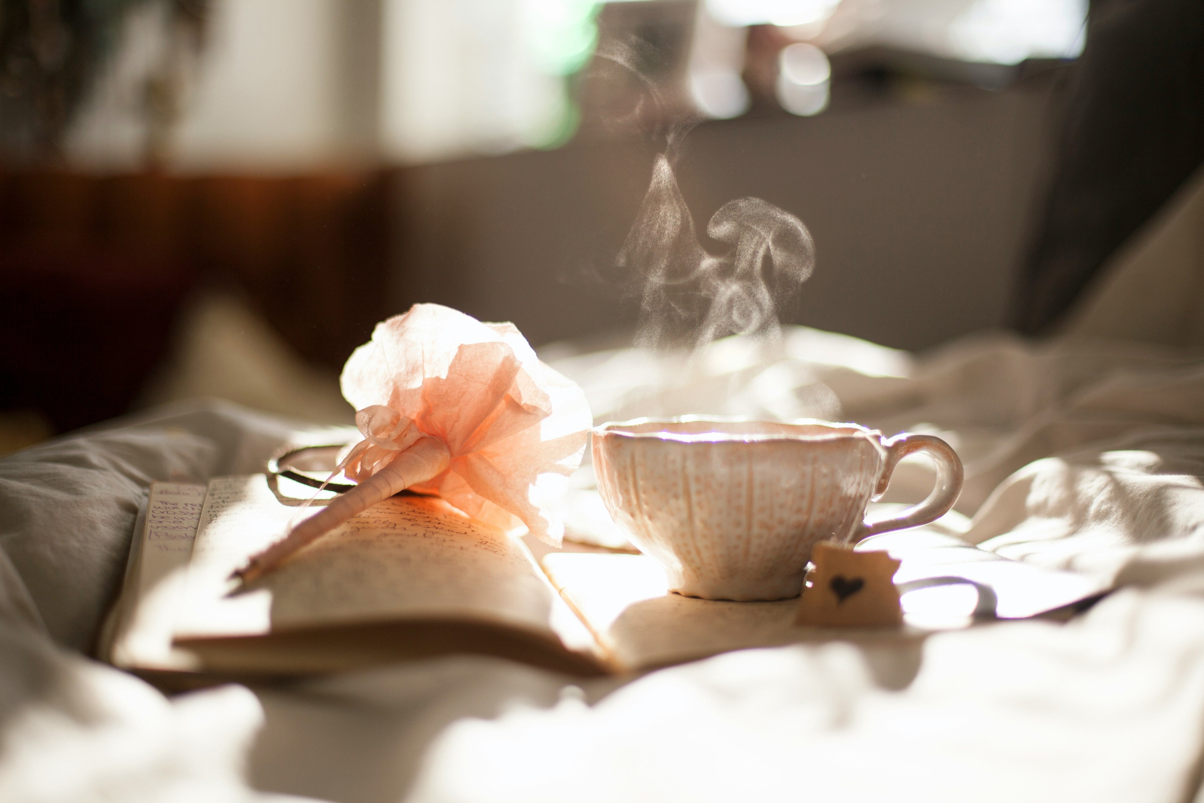 A handwritten gratitude journal beside a cup of tea and small seasonal flowers on a wooden table.