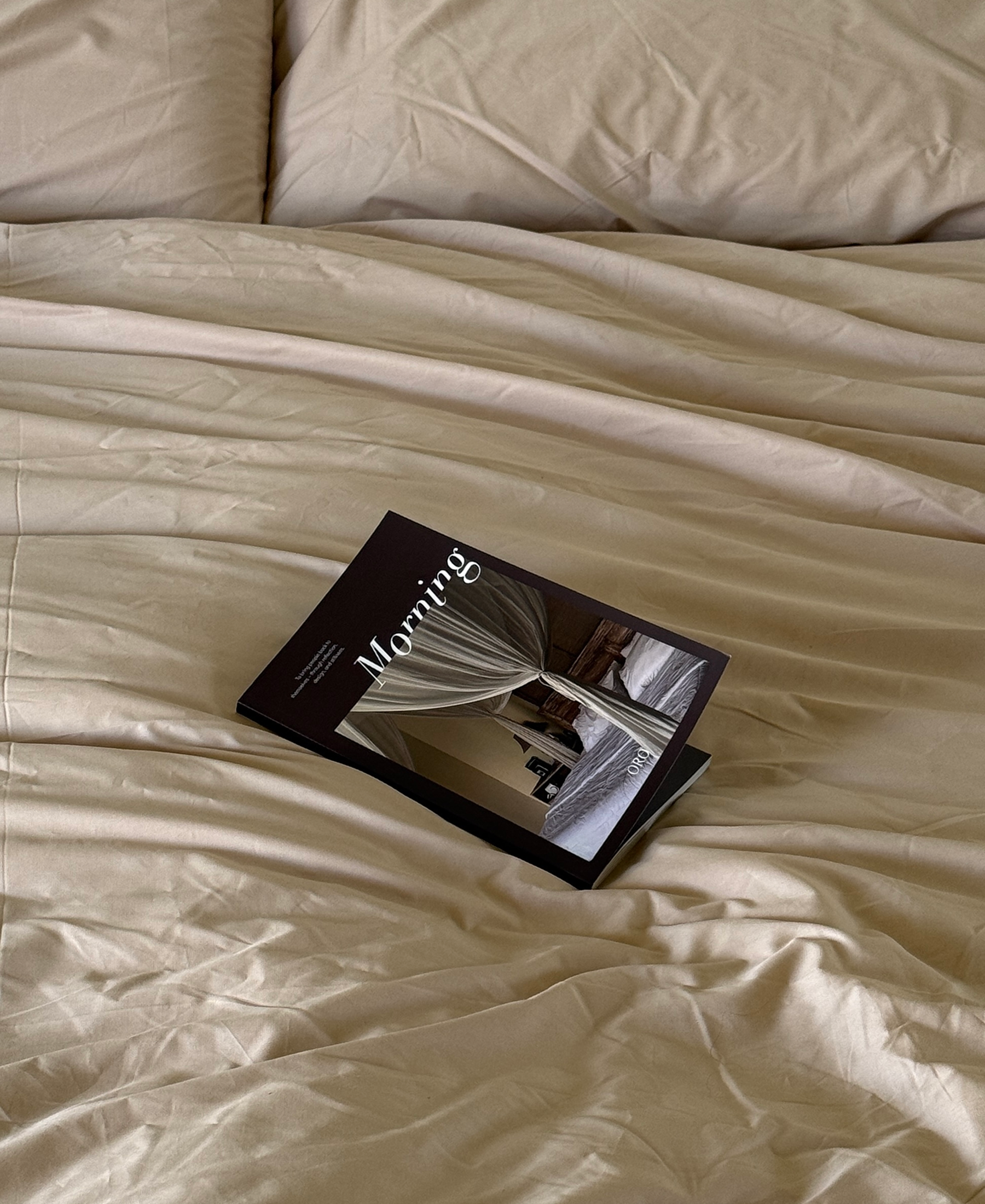 A magazine titled 'Morning' resting on rumpled beige bedding with pillows visible at the top.